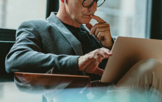 Ein Mann mit Brille nutzt einen Laptop in einem Café, um Strategien zur digitalen Neukundengewinnung umzusetzen.