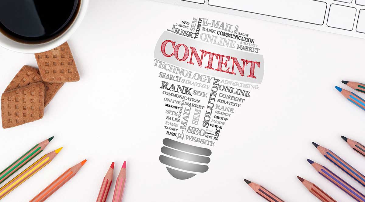 Eine Glühbirne auf einem Schreibtisch, zusammengesetzt aus mehreren Worten, das Wort „Content“ wird rot hervorgehoben –Symbolbild für Content produzieren.