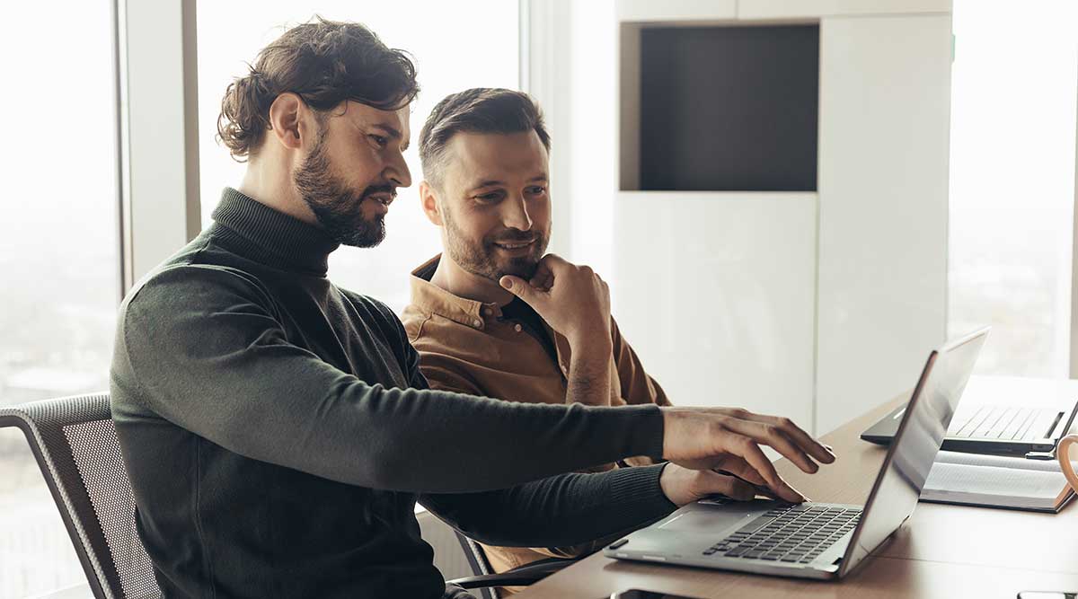 Zwei Männer sitzen an einem Schreibtisch, schauen auf einen Laptop und betreiben Marketing im Mittelstand.
