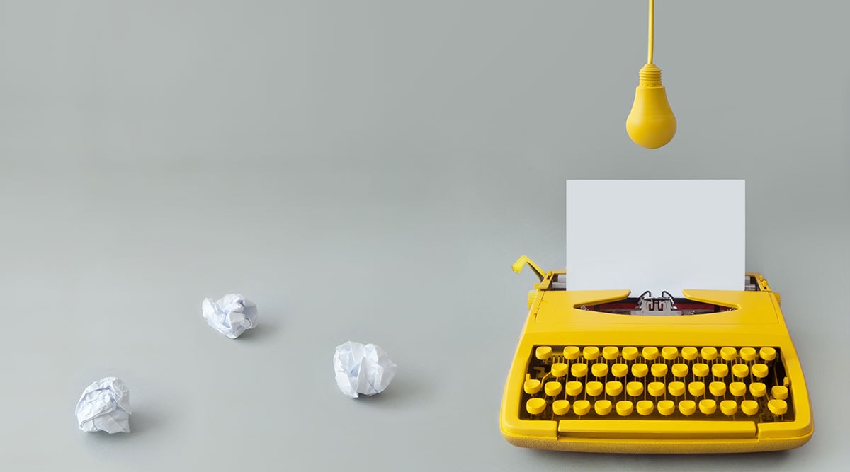 Eine gelbe Schreibmaschine mit einem weißen Blatt Papier und zerknülltem Papier: Symbolbild für Texte schreiben